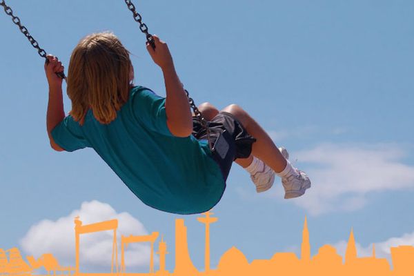 Schaukelndes Kind vor Kieler Skyline